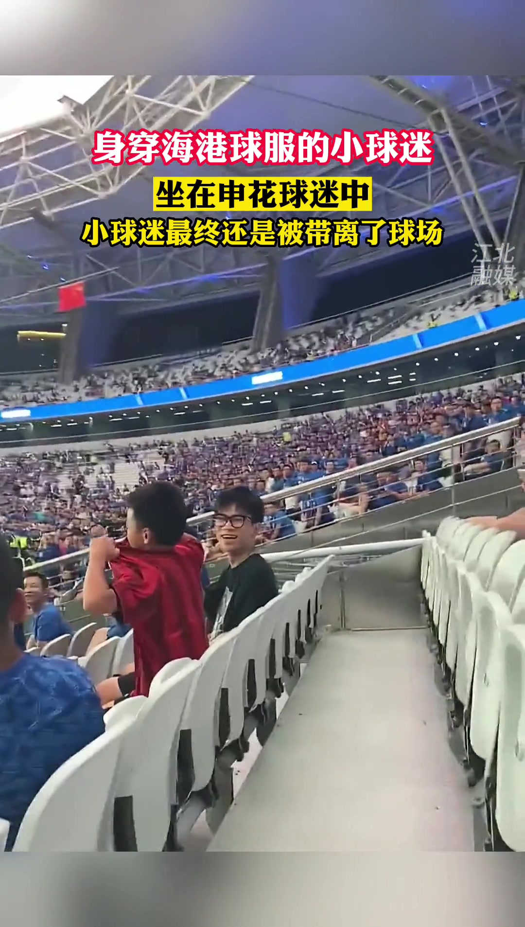 身穿海港球服的小球迷，坐在申花球迷中间被安保带离球场